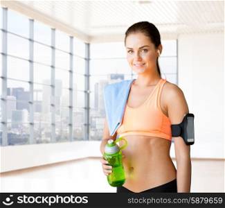 fitness, sport, drink and people concept - happy woman holding bottle of water, smartphone with earphones and towel over gym or home background