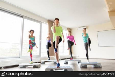 fitness, sport, exercising, aerobics and people concept - group of smiling people working out on step platforms in gym