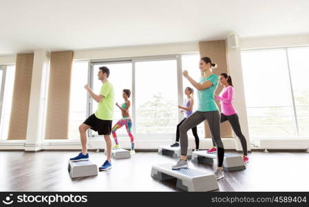 fitness, sport, exercising, aerobics and people concept - group of smiling people working out on step platforms in gym