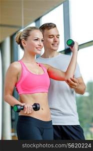 fitness, sport, exercising and diet concept - smiling young woman and personal trainer with dumbbells in gym