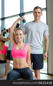 fitness, sport, exercising and diet concept - smiling young woman and personal trainer with dumbbell in gym