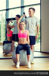 fitness, sport, exercising and diet concept - smiling young woman and personal trainer with dumbbell in gym