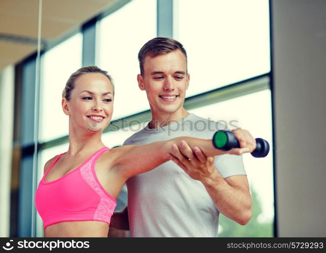 fitness, sport, exercising and diet concept - smiling young woman and personal trainer with dumbbell in gym