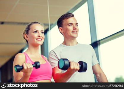 fitness, sport, exercising and diet concept - smiling young woman and personal trainer with dumbbells in gym