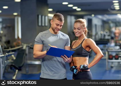 fitness, sport, exercising and diet concept - smiling young woman and personal trainer with clipboard writing exercise plan in gym