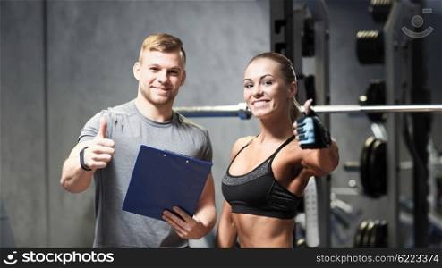 fitness, sport, exercising and diet concept - smiling young woman and personal trainer with clipboard showing thumbs up in gym