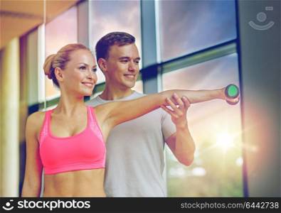 fitness, sport, exercising and diet concept - smiling young woman and personal trainer with dumbbell in gym. smiling young woman with personal trainer in gym