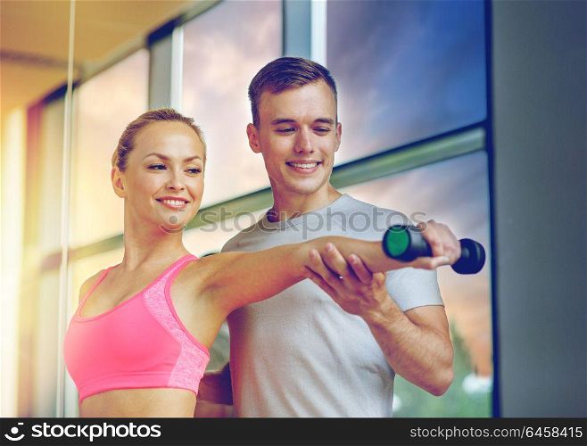 fitness, sport, exercising and diet concept - smiling young woman and personal trainer with dumbbell in gym. smiling young woman with personal trainer in gym