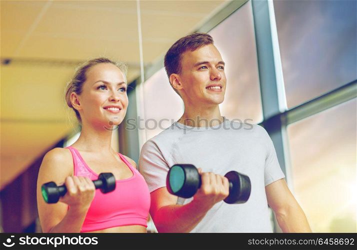 fitness, sport, exercising and diet concept - smiling young woman and personal trainer with dumbbells in gym. smiling young woman with personal trainer in gym