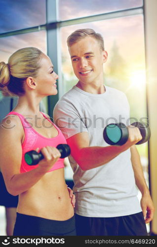 fitness, sport, exercising and diet concept - smiling young woman and personal trainer with dumbbells in gym. smiling young woman with personal trainer in gym