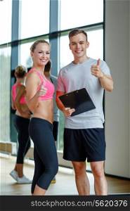 fitness, sport, exercising and diet concept - smiling young woman with personal trainer in gym showing thumbs up