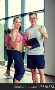 fitness, sport, exercising and diet concept - smiling young woman with personal trainer in gym showing thumbs up