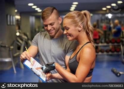 fitness, sport, exercising and diet concept - smiling young woman with personal trainer and exercise plan on clipboard in gym