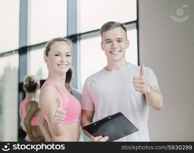 fitness, sport, exercising and diet concept - smiling young woman with personal trainer in gym showing thumbs up