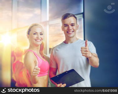 fitness, sport, exercising and diet concept - smiling young woman with personal trainer in gym showing thumbs up. smiling young woman with personal trainer in gym