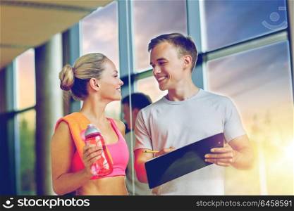 fitness, sport, exercising and diet concept - smiling young woman with personal trainer after training in gym. smiling young woman with personal trainer in gym