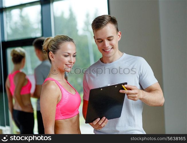 fitness, sport, exercising and diet concept - smiling young woman with personal trainer in gym