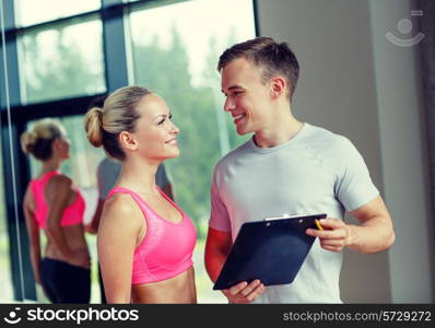 fitness, sport, exercising and diet concept - smiling young woman with personal trainer in gym