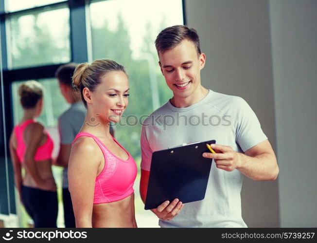 fitness, sport, exercising and diet concept - smiling young woman with personal trainer in gym