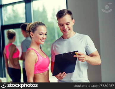 fitness, sport, exercising and diet concept - smiling young woman with personal trainer in gym