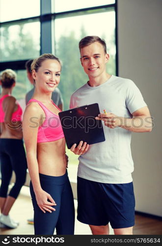 fitness, sport, exercising and diet concept - smiling young woman with personal trainer in gym