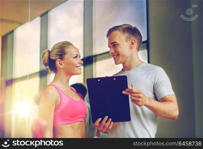 fitness, sport, exercising and diet concept - smiling young woman with personal trainer in gym. smiling young woman with personal trainer in gym