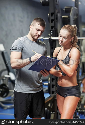 fitness, sport, exercising and diet concept - young woman and personal trainer with clipboard writing exercise plan in gym