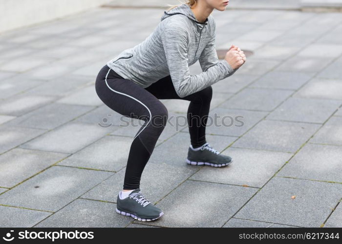 fitness, sport, exercising and healthy lifestyle concept - close up of woman doing squats outdoors