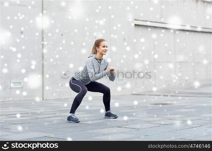 fitness, sport, exercising and healthy lifestyle concept - happy woman doing squats outdoors over snow