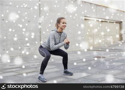 fitness, sport, exercising and healthy lifestyle concept - happy woman doing squats outdoors over snow