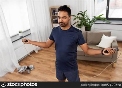 fitness, sport, exercising and healthy lifestyle concept - indian man skipping with jump rope at home. indian man exercising with jump rope at home