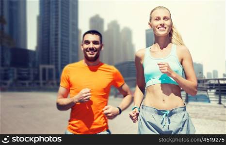 fitness, sport, exercising and healthy lifestyle concept - smiling couple running or jogging over dubai city street background