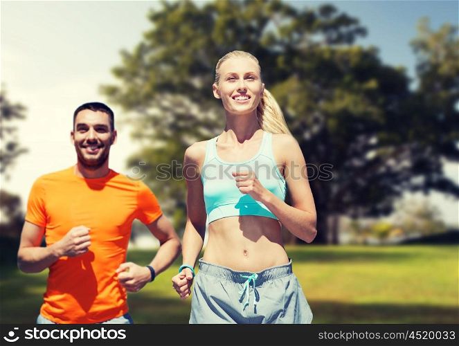 fitness, sport, exercising and healthy lifestyle concept - smiling couple running or jogging over summer park background