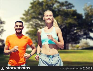 fitness, sport, exercising and healthy lifestyle concept - smiling couple running or jogging over summer park background