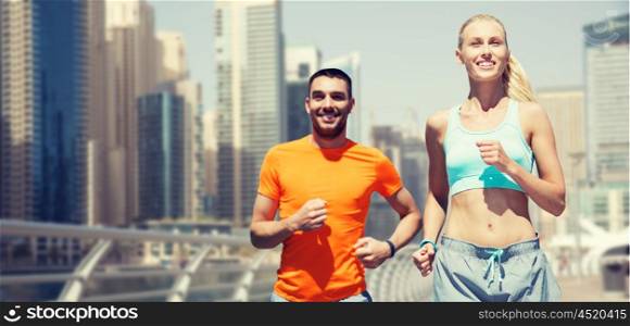fitness, sport, exercising and healthy lifestyle concept - smiling couple running or jogging over dubai city street background
