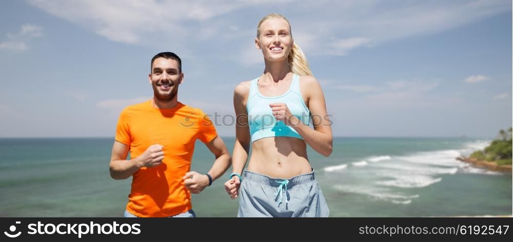fitness, sport, exercising and healthy lifestyle concept - smiling couple running or jogging over sea or beach background