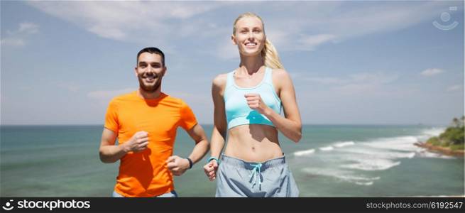 fitness, sport, exercising and healthy lifestyle concept - smiling couple running or jogging over sea or beach background