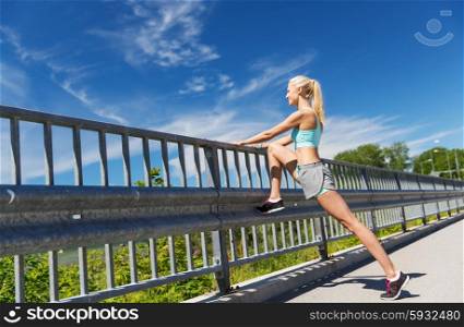 fitness, sport, exercising and healthy lifestyle concept - smiling woman stretching leg outdoors