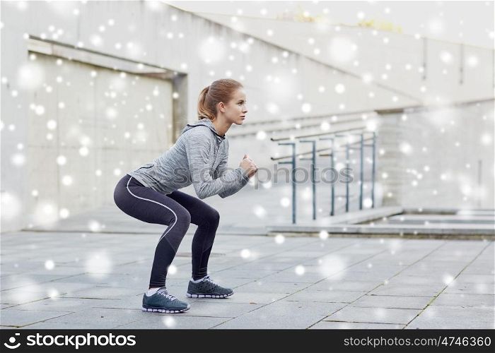 fitness, sport, exercising and healthy lifestyle concept - woman doing squats outdoors over snow