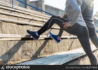 fitness, sport, exercising and lifestyle concept - close up of couple stretching leg on stands of stadium
