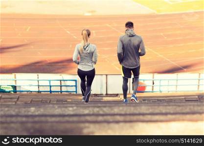 fitness, sport, exercising and lifestyle concept - couple running downstairs on stadium. couple running downstairs on stadium