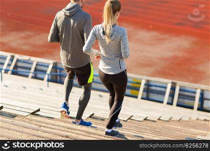 fitness, sport, exercising and lifestyle concept - couple running downstairs on stadium
