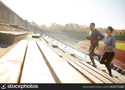 fitness, sport, exercising and lifestyle concept - couple running upstairs on stadium