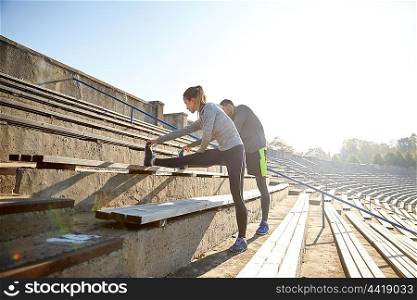 fitness, sport, exercising and lifestyle concept - couple stretching leg on stands of stadium