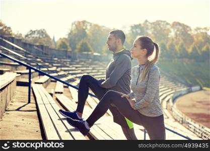 fitness, sport, exercising and lifestyle concept - couple stretching leg on stands of stadium. couple stretching leg on stands of stadium
