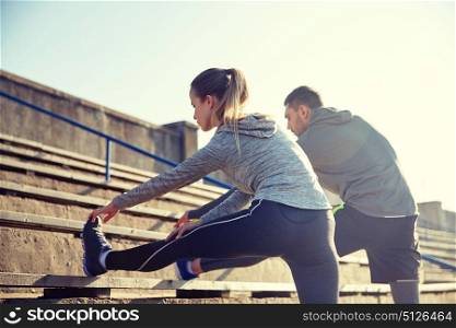 fitness, sport, exercising and lifestyle concept - couple stretching leg on stands of stadium. couple stretching leg on stands of stadium