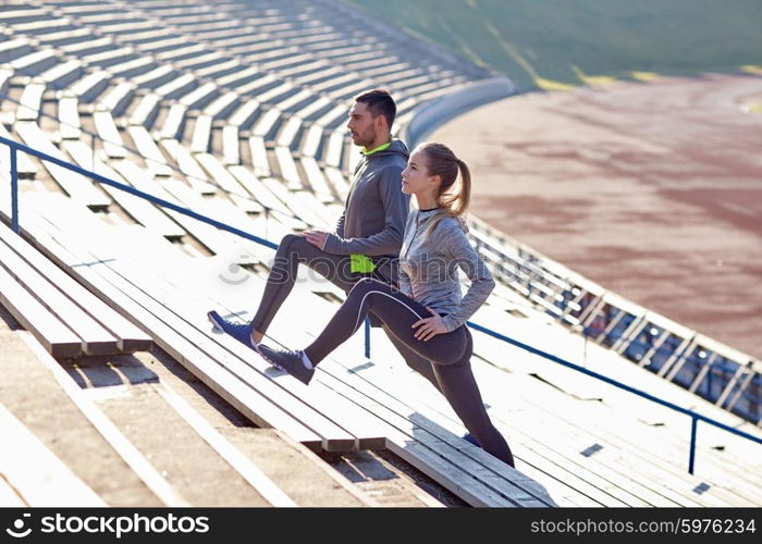 fitness, sport, exercising and lifestyle concept - couple stretching leg on stands of stadium