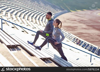 fitness, sport, exercising and lifestyle concept - couple stretching leg on stands of stadium