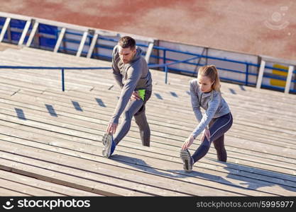 fitness, sport, exercising and lifestyle concept - couple stretching leg on stands of stadium