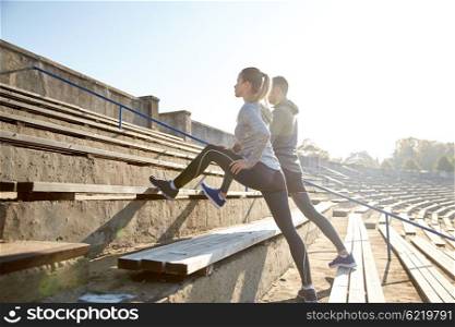 fitness, sport, exercising and lifestyle concept - couple stretching leg on stands of stadium